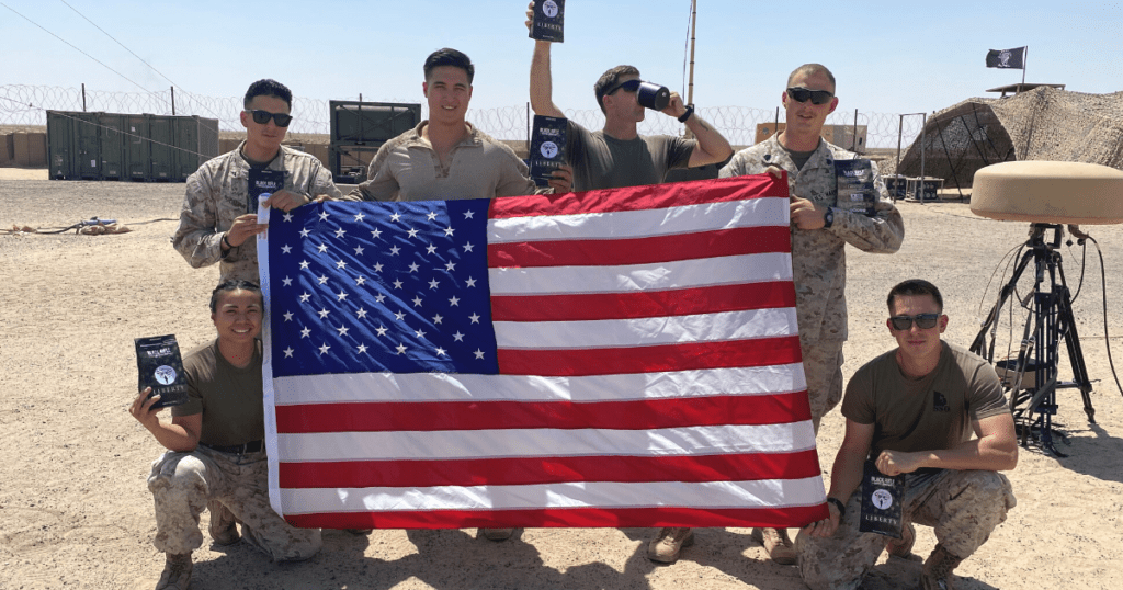 An image of deployed soldiers holding an American flag and items delivered from Soldiers' Angels